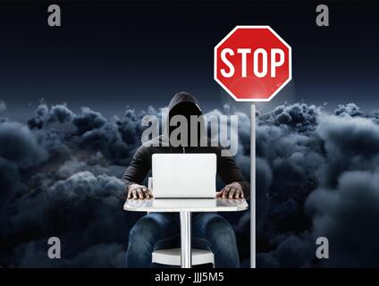 Hacker working on laptop close to a stop board in front of 3D cloudy background Stock Photo