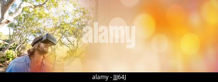 Man in forest with virtual reality headset looking up with orange bokeh transition Stock Photo