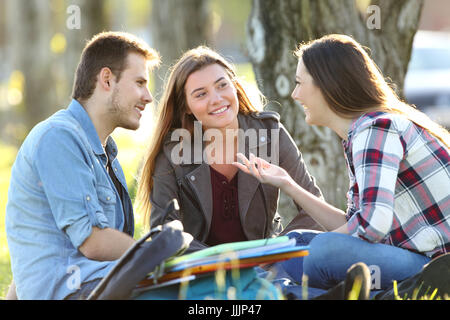 Three students talking after classes beside books and ruckpacks sitting on the grass in a park Stock Photo