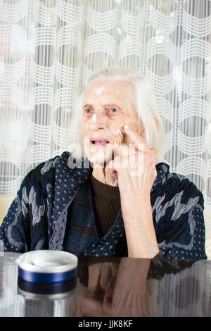 Senior woman applying face cream at home Stock Photo