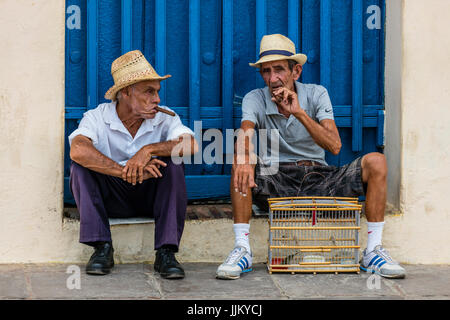 Older Cuban men smoking cigars in the PLAZA MAYOR - TRINIDAD, CUBA Stock Photo