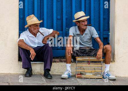 Older Cuban men smoking cigars in the PLAZA MAYOR - TRINIDAD, CUBA Stock Photo