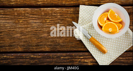 Orange slices in bowl with knife and napkin on table Stock Photo