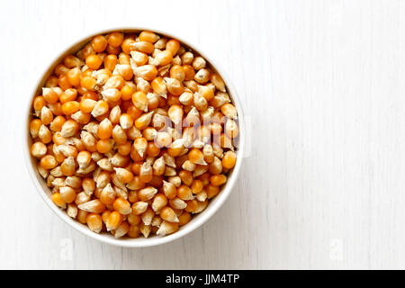 Unpopped popcorn  in white ceramic bowl isolated on painted white wood from above. Stock Photo