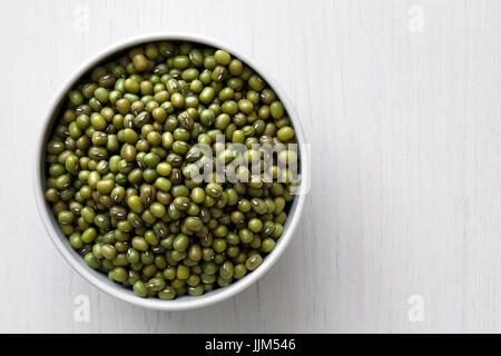 Dry mung beans  in white ceramic bowl isolated on painted white wood from above.