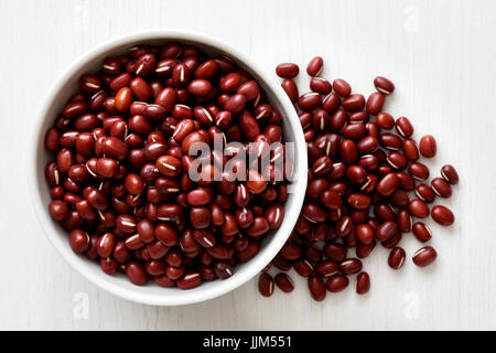 Dry adzuki beans  in white ceramic bowl isolated on painted white wood from above. Spilled beans. Stock Photo