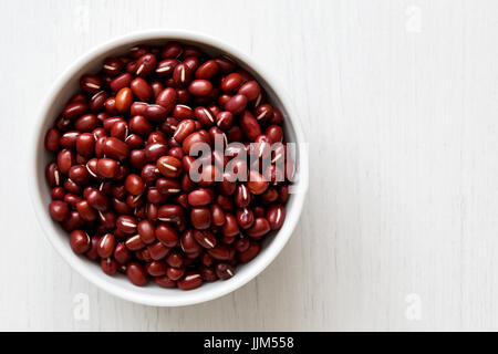 Dry adzuki beans  in white ceramic bowl isolated on painted white wood from above. Stock Photo