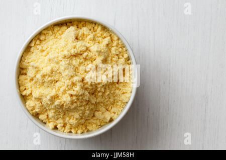 Corn flour  in white ceramic bowl isolated on painted white wood from above. Stock Photo