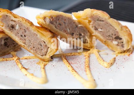 Homemade sausage in puff pastry displayed on a white plate with a mustard sauce design. Stock Photo