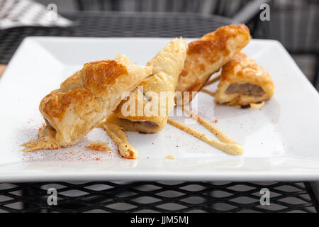 A twist on a pig in a blanket, artisan puff pastries stuffed with homemade sausage presented with mustard sauce. Stock Photo