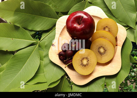 kiwifruit,apples and cherries on leaves background,focus at group of various winter fruit in wooden tray on green leaves background,sliced golden kiwi Stock Photo