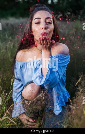 Red tinsel begins to fill the frame as my friend blows it from her hand during an outdoor portrait shoot near Liverpool. Stock Photo