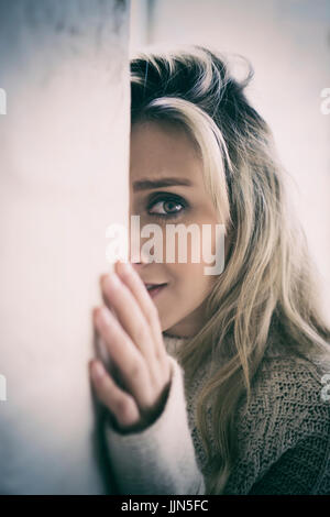Scared young woman in danger hiding behind the wall Stock Photo