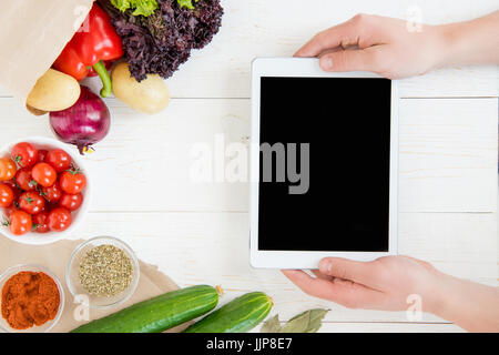 Close-up partial view of person using digital tablet with blank screen while cooking and fresh ingredients on wooden table Stock Photo