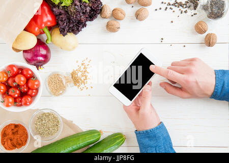 Close-up partial view of person using smartphone with blank screen while cooking and fresh ingredients on wooden table Stock Photo