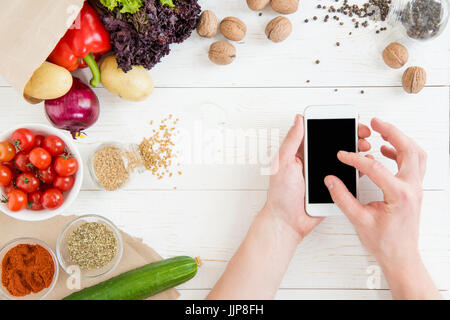 Close-up partial view of person using smartphone with blank screen while cooking and fresh ingredients on wooden table Stock Photo