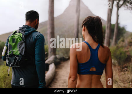 Rear view shot of healthy young couple walk through mountain trail. Young man and woman walking through country path. Stock Photo