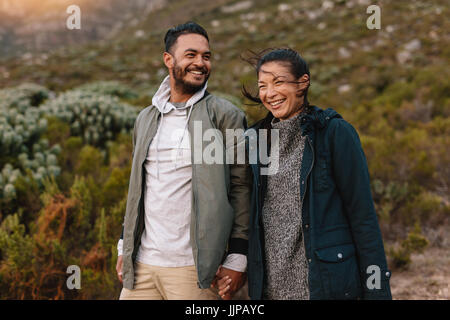 Portrait of smiling young couple walking in the countryside. Young man and woman hiking in nature. Stock Photo