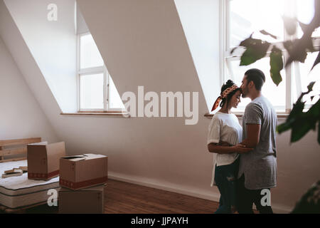 Indoor shot of loving young couple moving into their new home. Man and woman in love standing together with cardboard boxes in room. Stock Photo