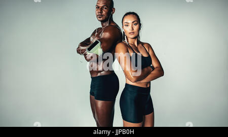 Portrait of beautiful athletic couple standing together on grey background. Muscular young man and woman with arms crossed looking at camera. Stock Photo