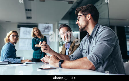 Young designer giving some new ideas about project to his partners in conference room. Business people discussing over new business project in office. Stock Photo
