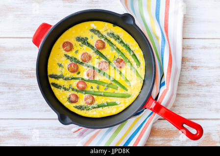 Top view of freshly made frittata with green asparagus and cherry tomatoes in a frying pan Stock Photo