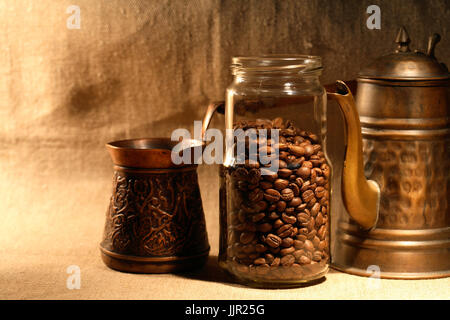 Glass jar with coffee beans near old copper coffeepot on canvas background Stock Photo
