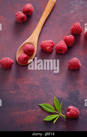 A fresh raspberry on a wooden spoon. Ripe fresh raspberries with leaves on rustic background. Stock Photo