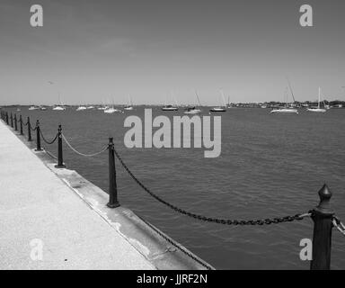B&W view from the boardwalk of St. Augustine Florida bay front near Castillo de San Marcos. Anchored sail boats face the same direction on the ocean. Stock Photo