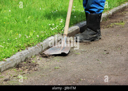 The worker removes the growing grass on a gravel path using an old shovel. Stock Photo