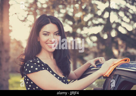 Young woman dry wiping her car with microfiber cloth after washing it, cleaning auto. Transportation self service, care concept. Stock Photo