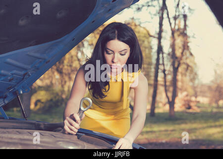 Portrait of a woman holding a wrench confidently with her broken down car on a rural park forest background Stock Photo