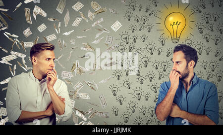 Side profile of two serious businessmen looking at each other one under money rain another with bright ideas Stock Photo
