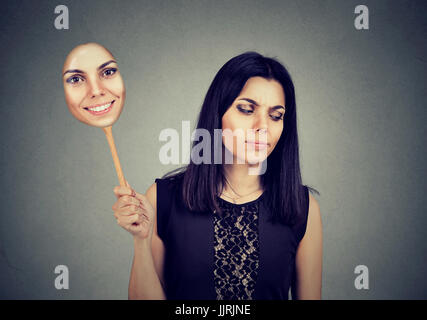 Young woman with sad expression taking of a mask expressing cheerfulness Stock Photo