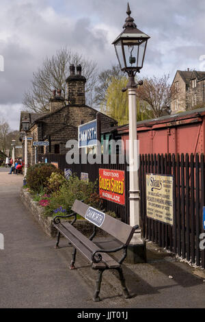 Looking along the quiet platform at quaint, historic Oakworth Station with gas lamps & retro adverts - Keighley and Worth Valley Railway, England, UK. Stock Photo