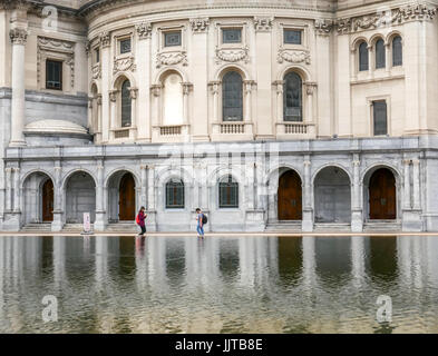 Two young people looking at their phones while walking past the Reflecting Pool, Christian Science Centre, Boston, Massachusetts  USA Stock Photo