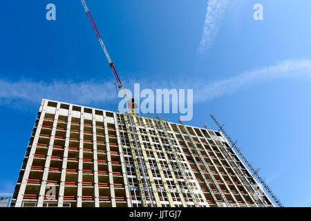 Low angle view of a concrete building under construction with a red and white tower crane at the top against blue sky. Stock Photo