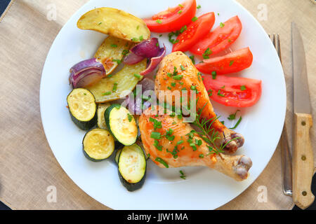 Roasted chicken legs with tomatoes, fingerling potatoes, onions, zucchini, rosemary and scallions on a white plate Stock Photo
