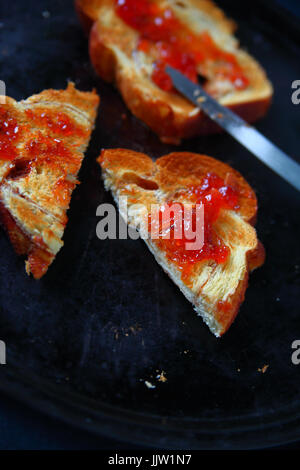 Slices of toast with raspberry jam, one cut in half, on a dark metal baking pan Stock Photo