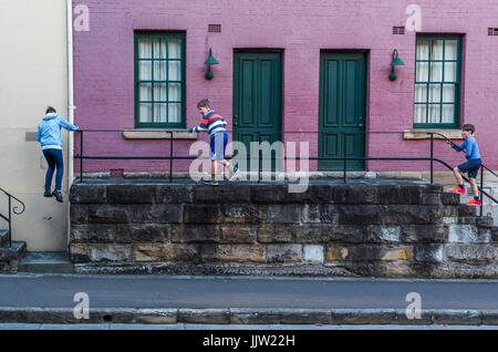 Three boys climbing on a staircase fence in front of a building at the Rocks in Sydney Australia Stock Photo