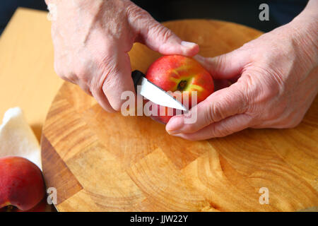 A man uses a paring knife to peel a fresh peach over a wood cutting board Stock Photo
