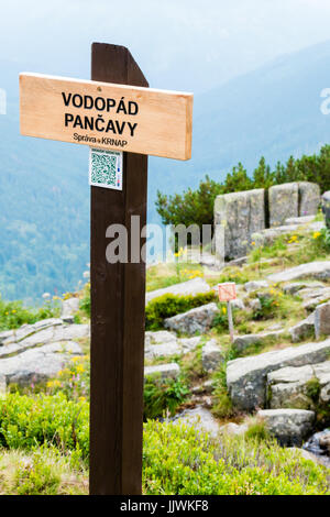 The wooden sign informs of Pancava Waterfall. On background, which is smooth blurry, there are, huge rocks, valley and faraway mountains. The sign is  Stock Photo