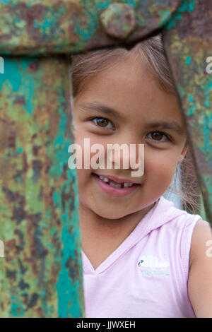 A smiling girl hiding behind an old hand water pump Stock Photo