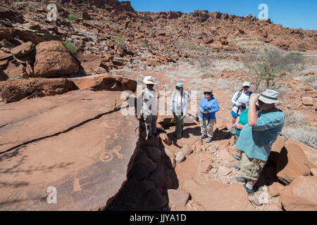 Tourists observing the rock carvings made by ancient tribes of Damaraland in Twyfelfontein, located in the southern region of Namibia, Africa. Stock Photo