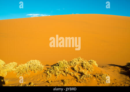 Distant view of tourists sitting and resting at the very top of Dune 45, located in the Sossusvlei pan of the Namib-Naukluft National Park in Namibia, Stock Photo