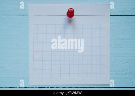 small square lined piece of paper pinned to the wooden board wall. blue background Stock Photo