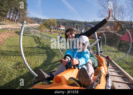 young excited mother and son enjoys driving on alpine coaster Stock Photo