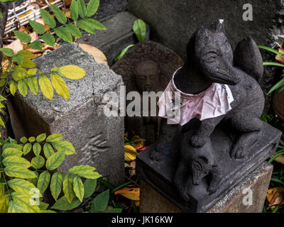 Sacred figurines, Kitsune fox guardian and buddhist statue, roadside shrine, Shinjuku, Tokyo, Japan Stock Photo