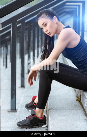 Young tired sportswoman in sportswear sitting on stadium stairs Stock Photo