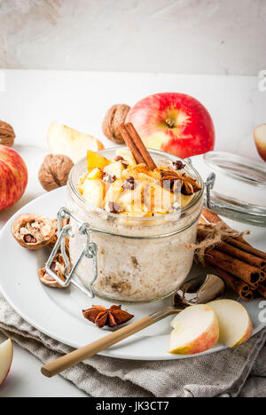 Healthy vegan food. Dietary breakfast or snack. Apple pie overnight oats, with apples, yogurt, cinnamon, spices, walnuts. In a glass, on a white marbl Stock Photo